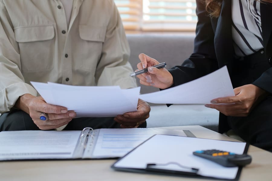 Two people reviewing documents together, with one holding papers and the other using a pen, on a table with a calculator.